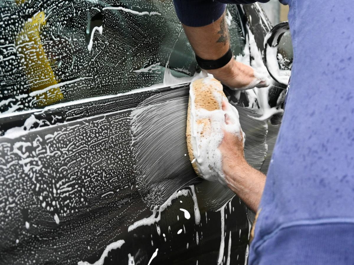 Hand washing a foam-covered car panel with a sponge